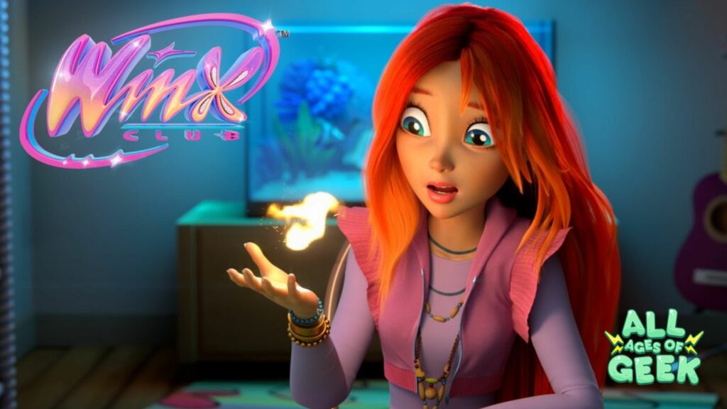 A promotional image for Winx Club featuring a red-haired character looking surprised at a small flame hovering above her hand. The background shows a cozy room with a glowing fish tank and a purple guitar. The logos for "Winx Club" and "All Ages of Geek" are prominently displayed.