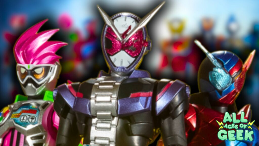 Three Kamen Rider characters are prominently featured in the foreground with vibrant colors. The character on the left has bright pink hair and a futuristic mask, the center character has a clock-themed helmet with red eyes, and the character on the right sports a blue and red helmet with a unique design. In the background, blurred figures of more Kamen Riders can be seen. The 'All Ages of Geek' logo is positioned at the bottom right corner.