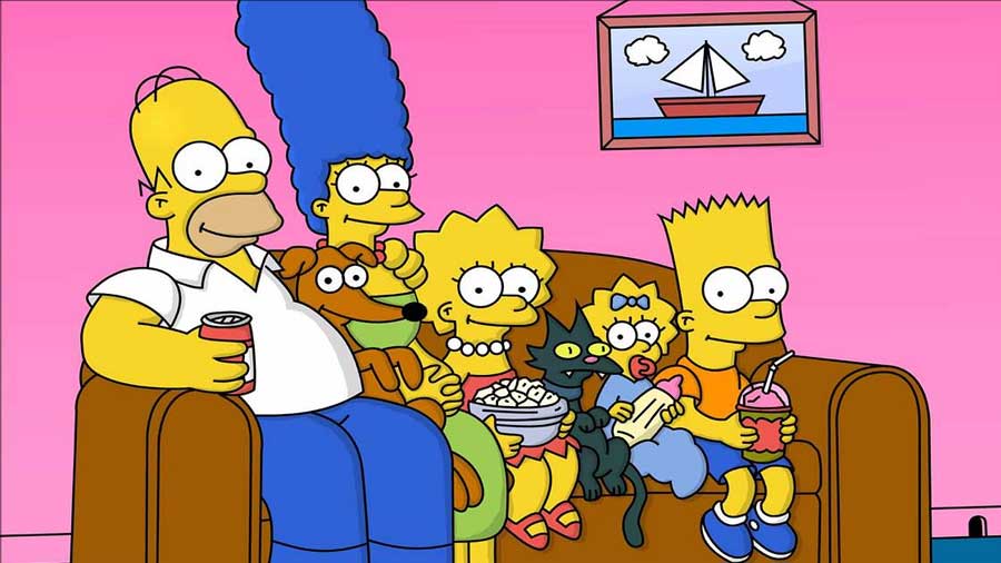 In the image, the iconic animated family from "The Simpsons" is sitting together on their living room couch. From left to right are Homer Simpson holding a can of soda, Marge Simpson with her tall blue hair, Lisa Simpson holding a bowl of popcorn, Maggie Simpson with her pacifier, and Bart Simpson sipping a drink. Their dog, Santa's Little Helper, and cat, Snowball II, are also present. The background features the familiar pink walls and a picture of a sailboat hanging on the wall. The family looks relaxed and happy, capturing the essence of this long-running, beloved show.