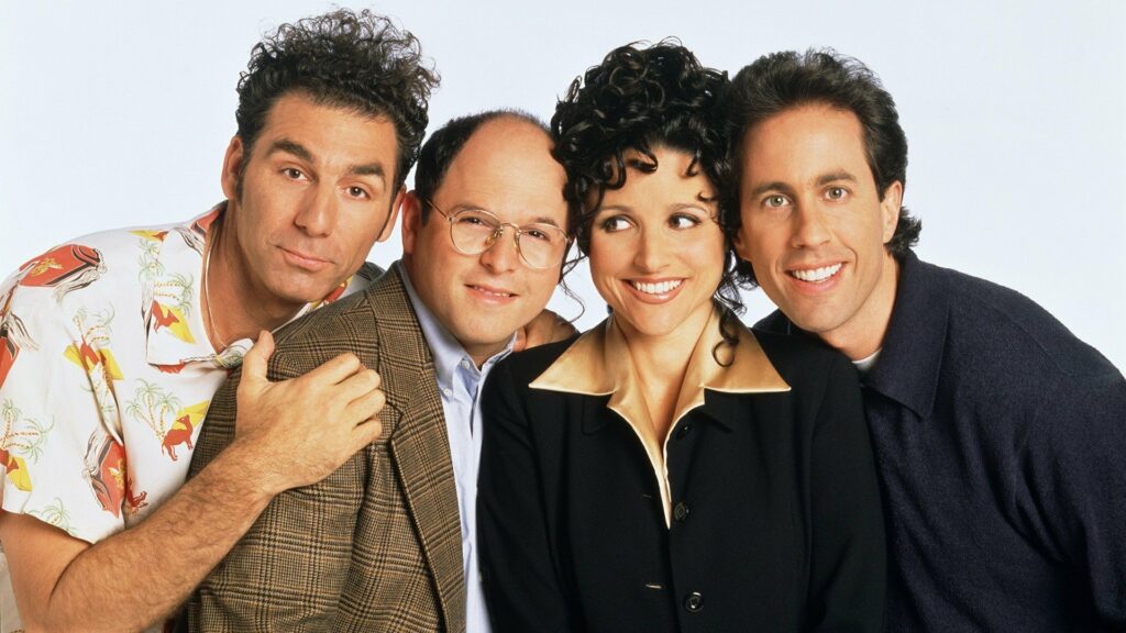 In the image, the main cast of the iconic 90s sitcom "Seinfeld" is shown together in a friendly and close pose. From left to right, the characters are Cosmo Kramer, George Costanza, Elaine Benes, and Jerry Seinfeld. Kramer is seen with his signature quirky expression, wearing a colorful Hawaiian shirt. George, dressed in a plaid blazer, looks more reserved but slightly amused. Elaine, with her curly hair and a big smile, exudes charm and confidence. Finally, Jerry, with his familiar bright smile, completes the group. The image captures the unique personalities and chemistry of the characters that made "Seinfeld" a beloved and timeless show.