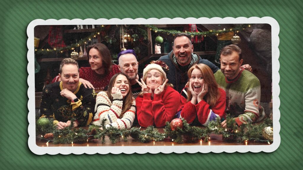 The image features the Critical Role Daggerheart Critmas cast, including Sam Riegel, Laura Bailey, Taliesin Jaffe, Ashley Johnson, Travis Willingham, Marisha Ray, Liam O’Brien, and Game Master Matthew Mercer. They are dressed in festive holiday sweaters, posing playfully with joyful expressions in front of a holiday-themed backdrop. The scene is decorated with garlands, Christmas lights, and ornaments, creating a cozy and cheerful atmosphere. The green textured border surrounding the image resembles a Christmas card, adding to the festive spirit of the Critical Role Daggerheart Critmas event.