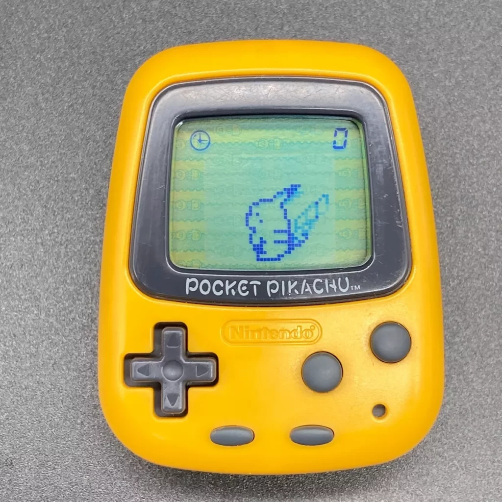 Close-up image of a yellow Pocket Pikachu, a virtual pet and pedometer device by Nintendo. The screen displays a pixelated image of Pikachu, and the device has a simple interface with a D-pad and two buttons below the screen. The words 'Pocket Pikachu' are printed beneath the screen, with the Nintendo logo also visible. The device has a small, rectangular shape, designed to be portable and easily carried in a pocket.