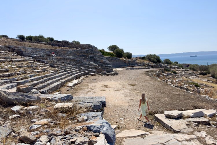 Abby exploring ancient Greek ruins near the coast, with a view of the sea in the distance.