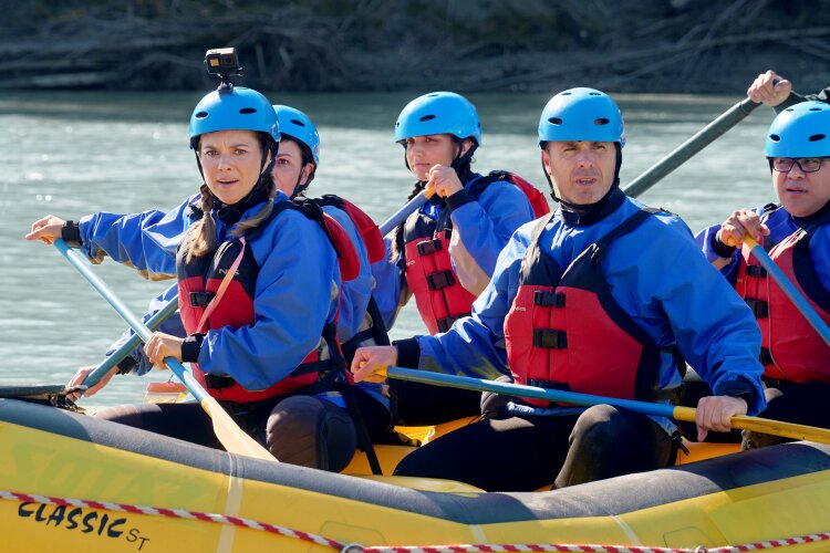 A close-up of a group of people in blue helmets and life jackets paddling a yellow raft, with focused expressions as they navigate the river. From Hallmark's "A Whitewater Romance".