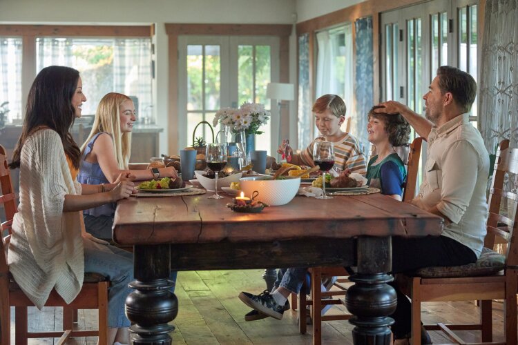 A family sitting around a dinner table, enjoying a meal and each other’s company. From Hallmark's "Big Sky River: The Bridal Path" ​
