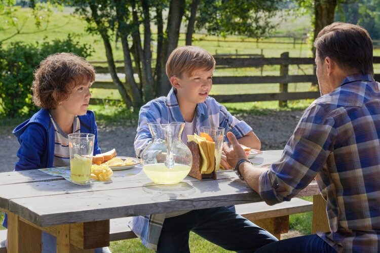  A man and two children sitting at an outdoor table, talking and enjoying lemonade. From Hallmark's "Big Sky River: The Bridal Path" ​