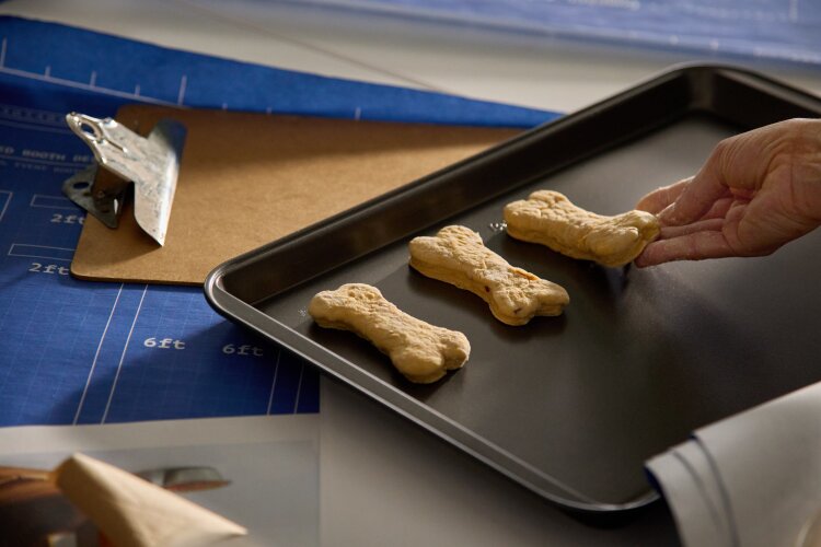 A tray of bone-shaped dog treats being placed on a baking sheet.