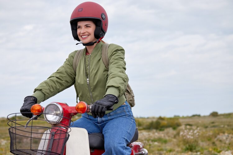  A woman wearing a helmet and riding a red scooter, smiling happily. From Hallmark's "For Love & Honey"
