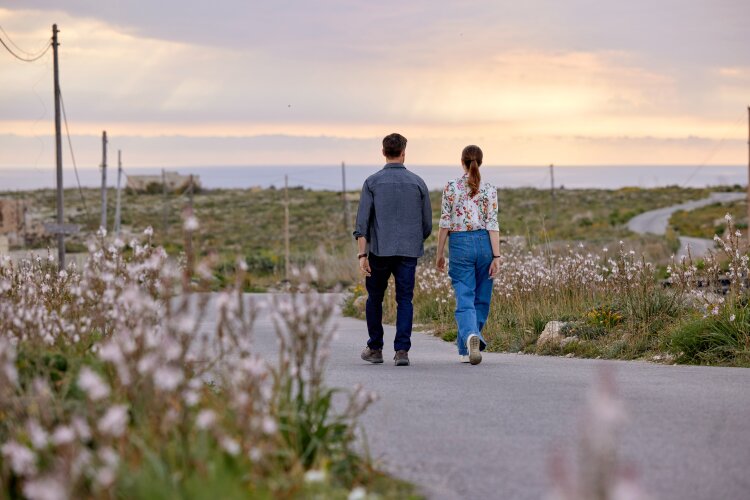  A man and a woman walking down a road towards the sunset, with wildflowers on the sides. From Hallmark's "For Love & Honey"

