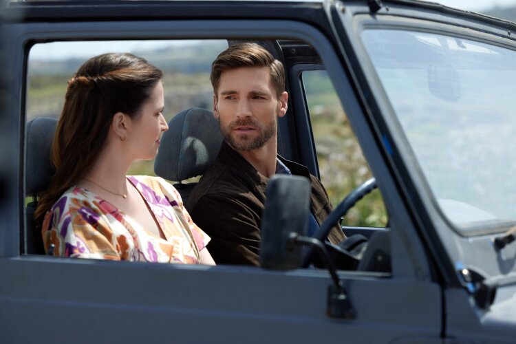 A man and a woman sitting in a car, looking at each other thoughtfully. From Hallmark's "For Love & Honey"
