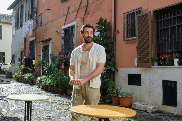 A man standing in an Italian street, casually leaning on a table with a relaxed expression.  "Two Scoops of Italy"  on Hallmark.