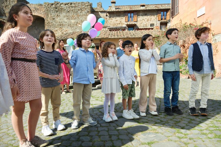  A group of children holding colorful balloons, excitedly looking at something off-camera.  "Two Scoops of Italy"  on Hallmark.