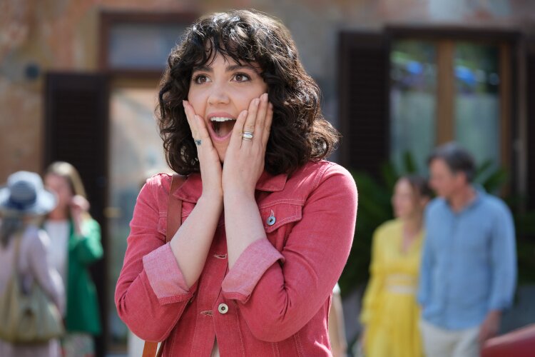 A woman with curly hair expressing surprise and joy, with her hands on her cheeks.