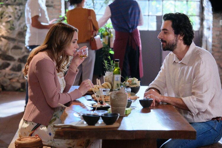 A man and woman sitting at a rustic wooden table in a cozy restaurant, enjoying a meal together.  "Two Scoops of Italy"  on Hallmark.