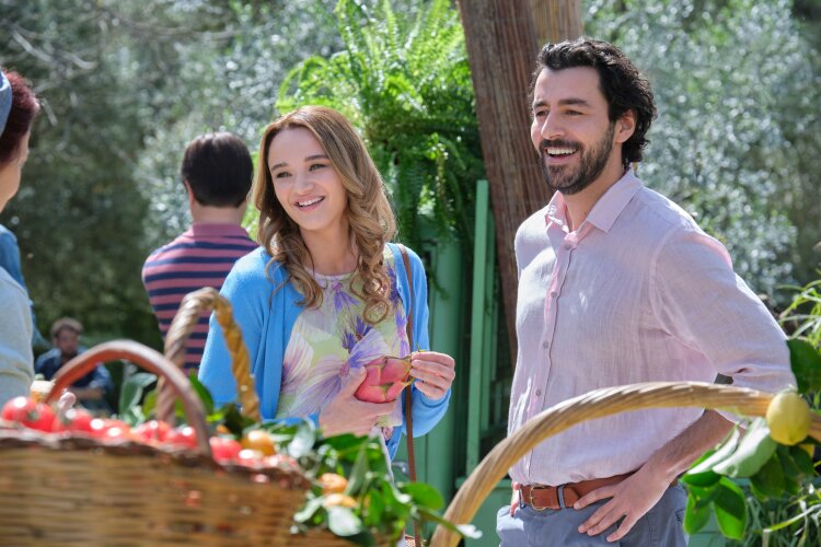  A couple smiling and enjoying a sunny day at an outdoor market, surrounded by fresh produce and greenery.