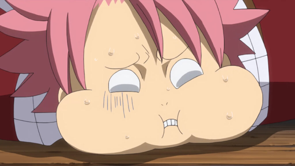 Natsu from Fairy Tail with puffed up cheeks his body planted on the floor looking pukey and sick.