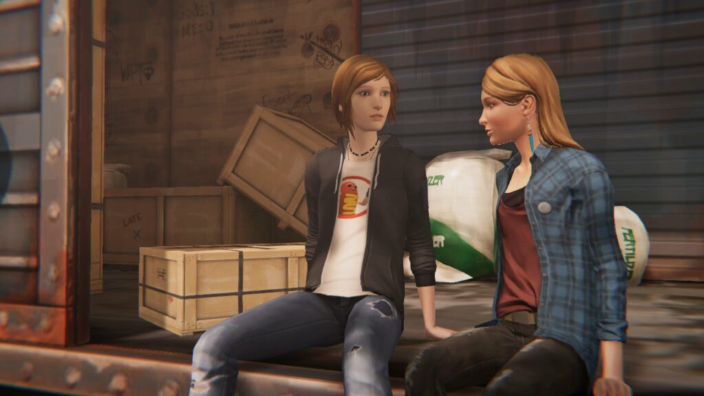 Chloe and Rachel sit on a cargo train looking intrigued at each other, Chloe dressed in a black jacket and jeans while Rachel wears jeans and a blue flannel shirt.