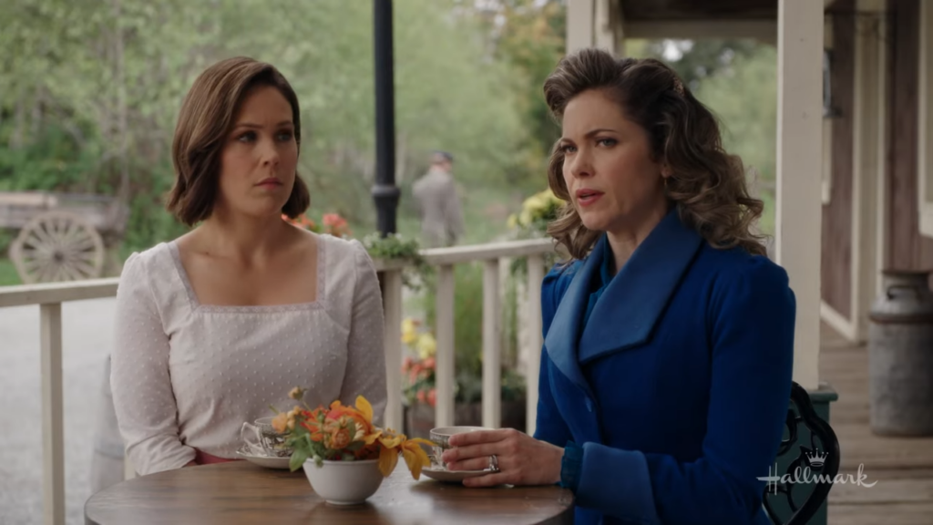 Elizabeth and Rosemary having a conversation: Elizabeth, in a white dress, and Rosemary, in a blue coat, are seated at an outdoor table having a serious conversation. "Run to You When Calls the Heart"