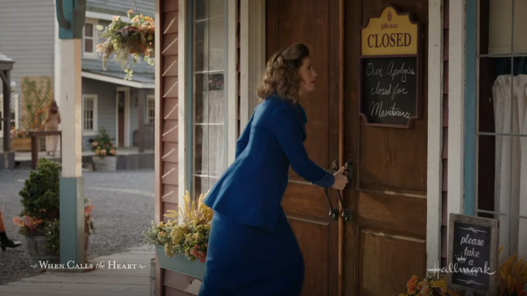 Rosemary in a blue coat, is unlocking the door of a closed building, with a "Closed for Maintenance" sign visible.