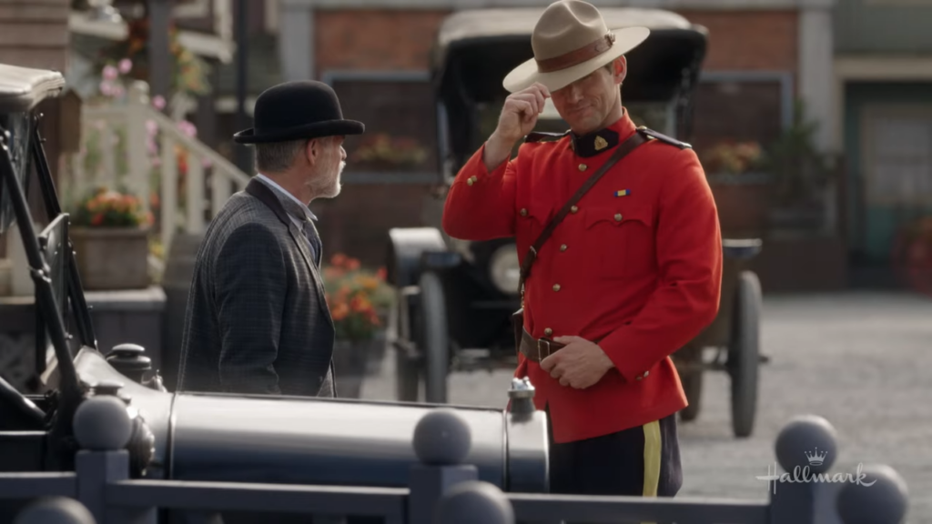 Nathan Grant tipping his hat: Nathan Grant, in his red Mountie uniform, tips his hat to a man in a gray suit and bowler hat beside a vintage car. "Run to You When Calls the Heart"