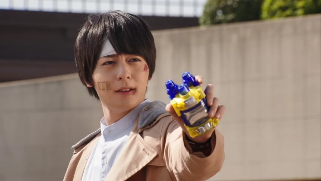 Sento Kiryu from Kamen Rider Build holding a transformation device, with bandages on his face and looking determined.