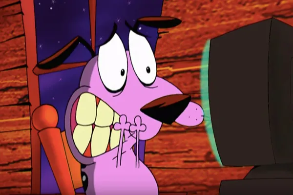 An animated scene featuring Courage from 'Courage the Cowardly Dog.' Courage, a pink dog, has a frightened expression with wide eyes, clenched teeth, and paws held close to his mouth. He is sitting on a chair in front of a glowing computer screen. The background shows a wooden wall typical of his farmhouse setting.