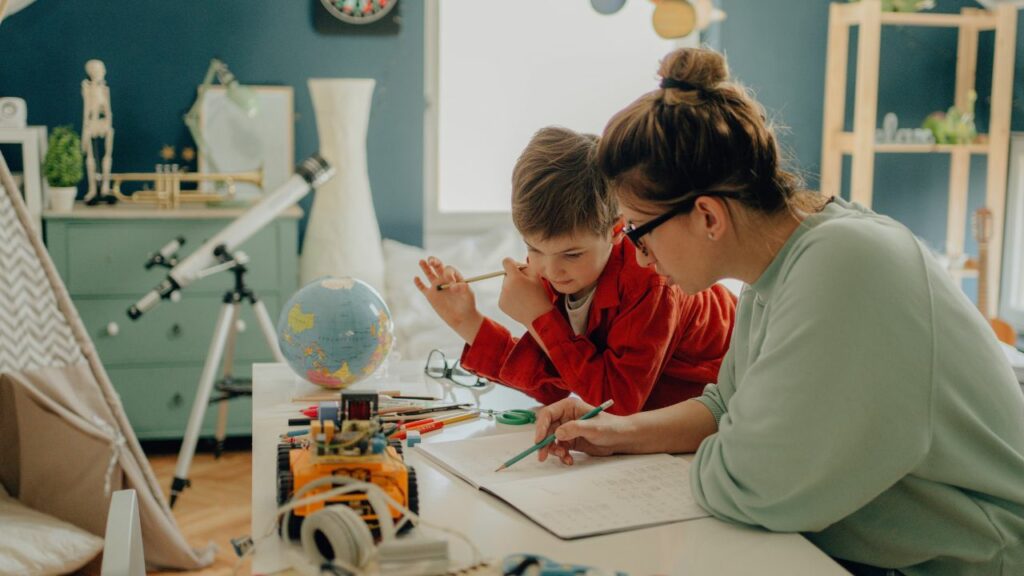 A calm and organized learning environment can significantly enhance the homeschooling experience. This image shows a parent and child engaged in a study session, surrounded by educational tools like a globe, telescope, and various stationery. The tidy room and focused atmosphere demonstrate how a well-structured space can facilitate concentration and effective learning, making homeschooling both productive and enjoyable.