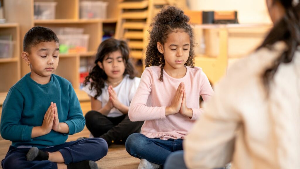 Practicing mindfulness can significantly benefit homeschooled children by enhancing their focus and emotional well-being. This image captures children engaged in a mindfulness exercise, seated calmly with their hands together and eyes closed. Such activities can help create a serene learning environment, promote self-awareness, and reduce stress, contributing to a balanced and productive homeschooling experience.