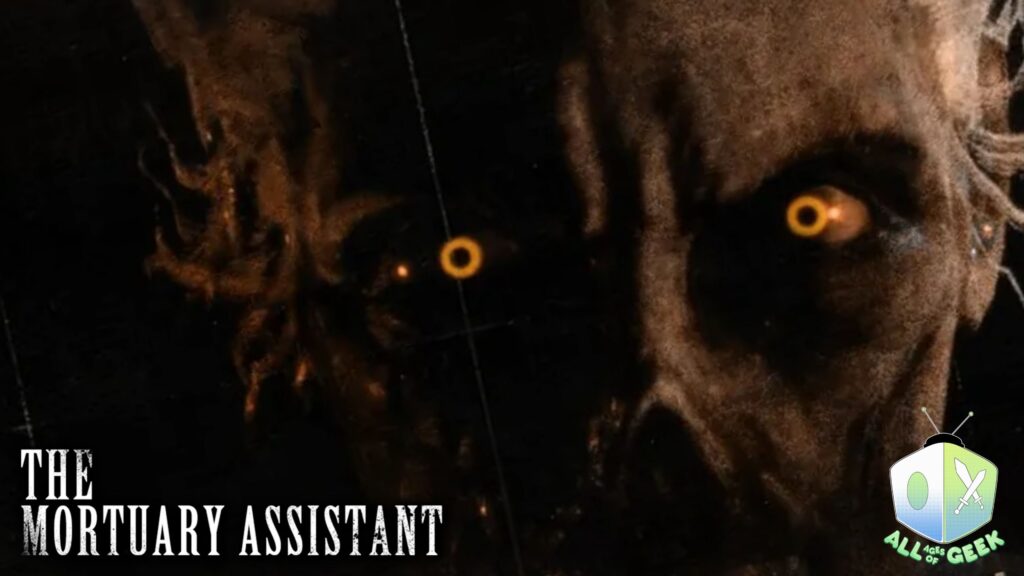 The Mortuary Assistant featured on All Ages of Geek. The thumbnail captures the corpse from The Mortuary Assistant with topaz eyes. The Mortuary Assistant logo is on the left hand lower side. The All Ages of Geek logo is on the lower right hand side indicating the publication.