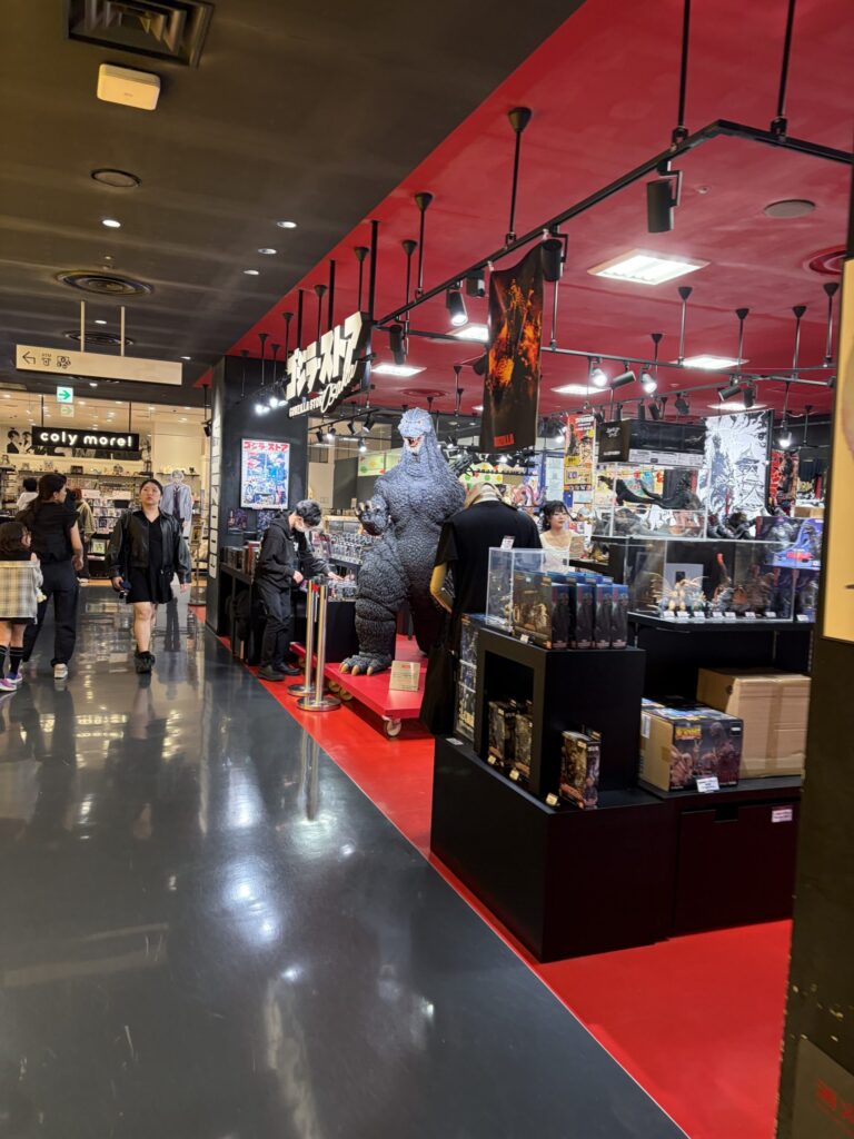 Wide view of the Godzilla Store Osaka inside Shinsaibashi PARCO, showcasing a large Godzilla statue, red and black interior design, and shelves filled with Godzilla merchandise.