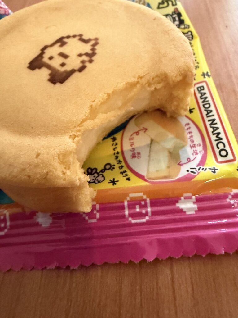 A Tamagotchi Manmaruyaki dessert with a bite taken out, showing the creamy milk filling inside the soft golden dough.