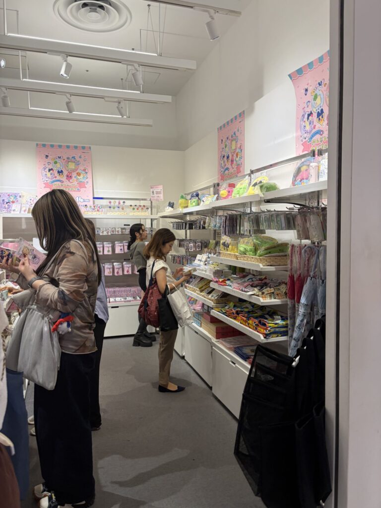 Customers and staff interacting at the checkout area surrounded by pastel Tamagotchi displays and plushies.